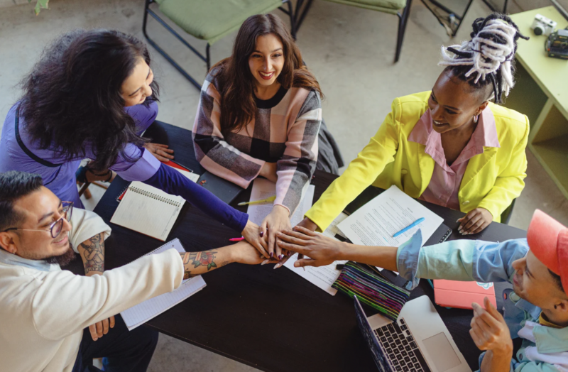 company culture -teamwork - employees putting their hands together in a team huddle