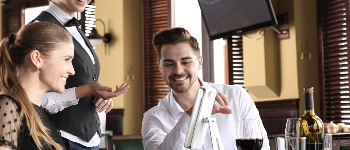 waitress explaining to couple how to use ordering kiosk at restaurant table